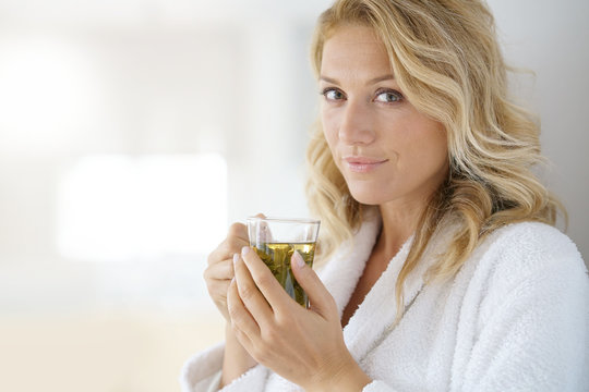 Portrait of attractive 40-year-old woman in bathrobe drinking infusion