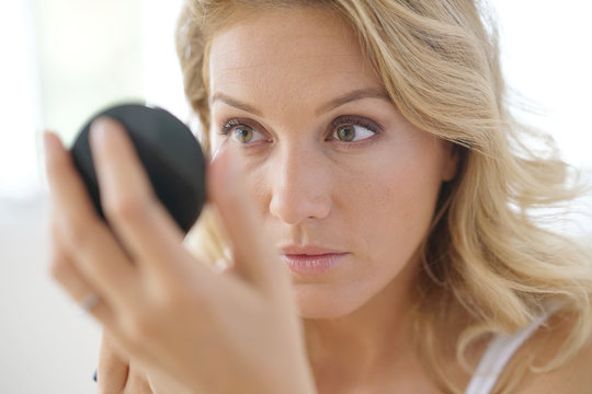 Portrait of attractive blond woman putting makeup on