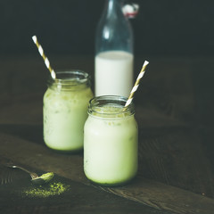 Cold refreshing iced coconut matcha latte drink in glass jars. Selective focus, copy space, dark background, square crop. Clean eating, healthy, vegetarian, alkaline diet, dairy free food concept