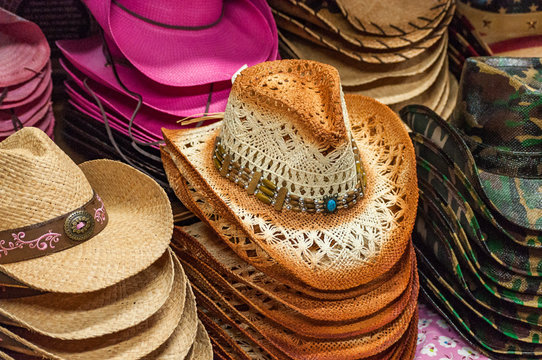 It's All About The Hat.  An image of a display of ladies cowboy hats arranged in neat stacks on a floral print table top featuring fancy embellishments, hat bands, jewelry and fancy woven patterns.