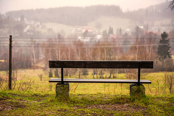 Fototapeta premium Old wooden bench in a rainy and foggy day in mountains. Eternal autumn. Fall. Autumn mood