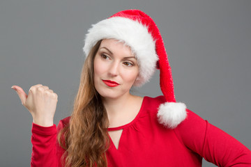 Junge Frau mit Weihnachtsmütze zeigt mit dem Finger zur Seite
