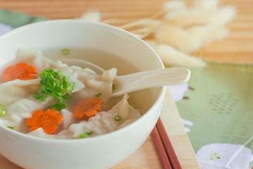 Close up minced pork wonton soup in white bowl on wood cutting board on wood table. Homemade delicious wonton in clear soup for breakfast or lunch or dinner.Wonton soup is always popular Chinese food.