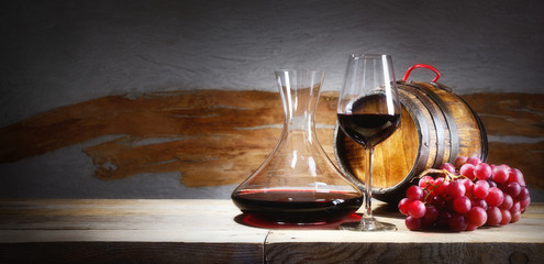 Red wine glass with bunch of grapes, decanter and small barrel