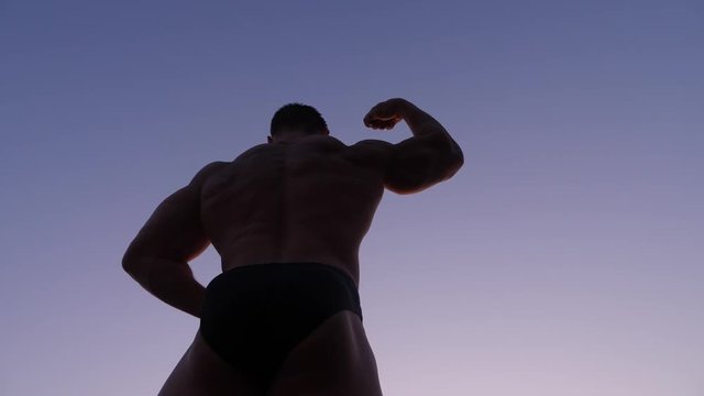 silhouette of a male bodybuilder. beautiful athlete posing on the beach at sunset. 4k. slow shooting