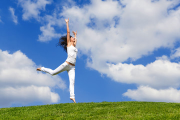 Happy young woman jumping on green grass. Landscape of grass field on bright sunny day. Nature beauty background, blue cloudy sky and summer green meadow. Outdoor lifestyle. People freedom concept