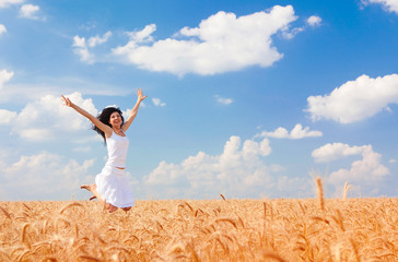 Naklejka na ściany i meble Happy woman jumping in golden wheat, enjoying the life in the field. Nature beauty, blue cloudy sky and field of wheat. Happy outdoor lifestyle. Freedom concept. Woman in summer field