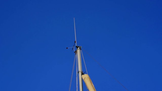 Sailing boat main mast close-up. Wind blowing and turning windex against clear blue sky. In slow-motion hd.