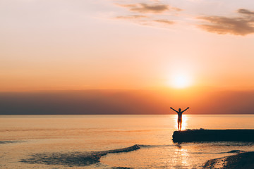 Young woman standing with raised arms looking in sunset