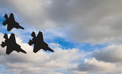 Silhouettes of three F-35 aircraft against the blue sky and white clouds