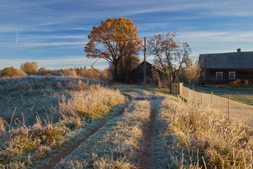 The first frost in autumn, rural landscape with wooden house and track
