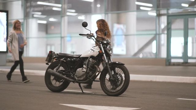 Two beautiful young women riding a motorcycle at night on city street and talking to each other. Female biker with his girlfriend