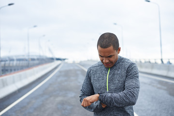 Serious young African American athlete checking burned calories on electronic smart watch application after cardio workout outdoor session. Male runner looking at smart watch heart rate monitor