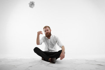 People, business, job and occupation. Tired overworked young businessman with fuzzy beard doing paperwork, sitting on floor in office, surrounded with documents and throwing crumpled paper at camera