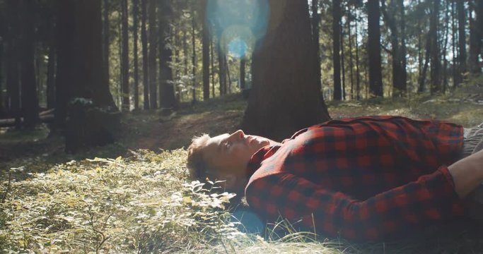 Handsome young man lying on the ground and resting from hard-working day in the park. Man in checkered shirt resting in a forest.