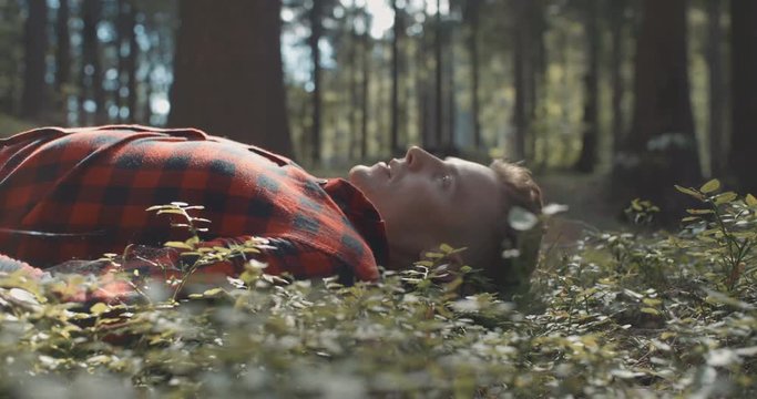 Handsome young man lying on the ground and resting from hard-working day in the park. Man in checkered shirt resting in a forest.