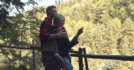 Rear view of hugging couple standing on a hill in a forest. Adventure, travel, tourism, leisure and love concept -  loving couple watching beautiful view.