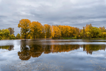 Obraz premium The lake, reflecting the cloudy sky and autumnal foliage trees