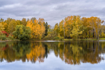 The lake, reflecting the cloudy sky and autumnal foliage trees