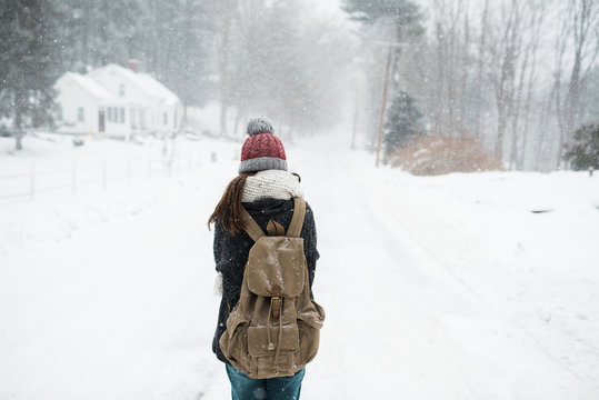 woman walking down a snowy road with backpack