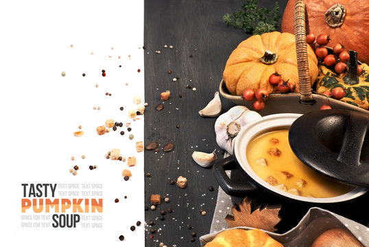 Pumpkin creme soup iserved with croutons in a dark ceramic pan, space