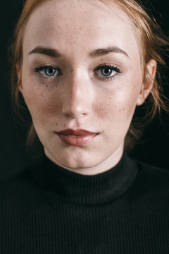 Closeup portrait of a ginger freckled woman on black.