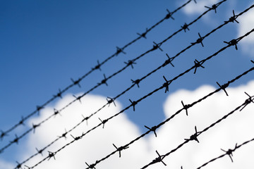 Black barbed wires over cloudy blue sky