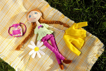 Textile handmade doll toy teenager girl with blue eyes and a flower of a camomile lie on blanket on grass. Top view