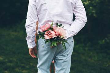 man holding a peony bouquet behind his back