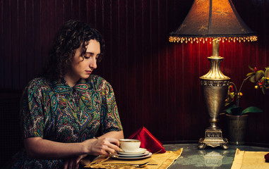 A 1950s period portait of a young sophisticated woman drinking tea in a cafe
