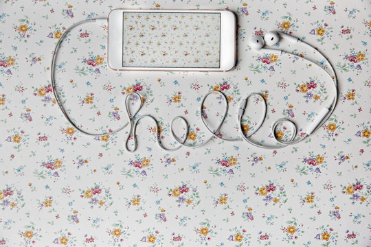 Mobile phone on a floral pattern with hello written with cable