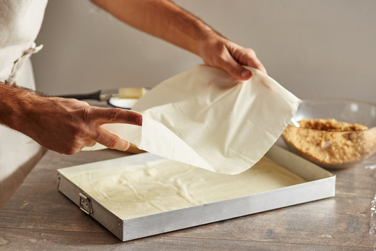 Man placing filo sheets into baking pan