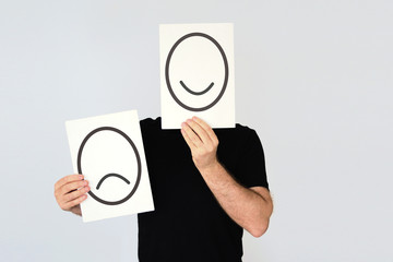 Man holding two cards with happy and unhappy faces drawn representing different options. Duality...