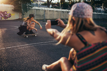 Happy young girl skateboarding with friend taking photos