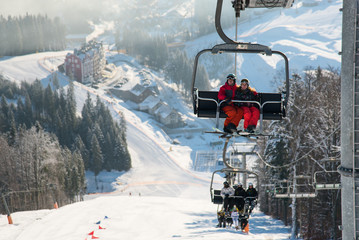 Skiers on the ski lift riding up at ski resort with beautiful background of snow-covered slopes, forests, hills in Bukovel, Ukraine