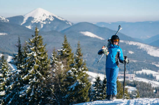Happy female skier standing on top of a mountain with skis on her shoulder stunning scenery. Mountains, forests on the background copyspace winter snow mountains nature recreation resort