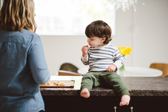 Young toddler sitting on counter eating fruit with his mother