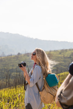 Beautiful young woman photographer hiker taking a photo on the top of a mountain peak