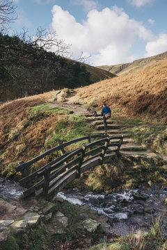Male and his dog crossing an old wooden bridge on a hillside. Edale, Derbyshire, UK.
