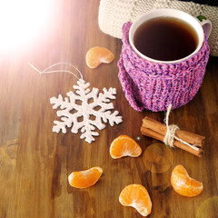 Tea in a mug wrapped into tiny scarf surrounded by mandarin segments. Photo with special editing