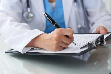 Fototapeta premium Doctor woman filling up medical form while sitting at the table, close-up of hands