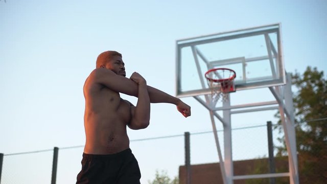 african american sporty man with naked torso warming up in morning on basketball court slow motion 