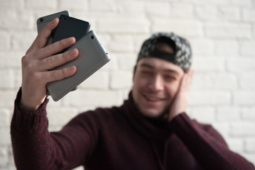 smiling young man looks at three different smartphones in his hand making selfie