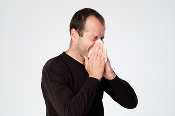 Mature man is ill from colds or pneumonia, sneezing in napkin.
