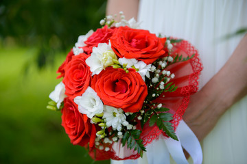Wedding bouquet in hands of bride. Scarlet red roses in a big, fancy bouquet. The details of the wedding accessories.