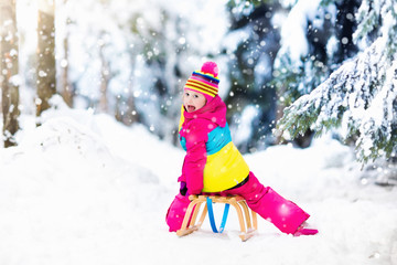 Child playing in snow on sleigh in winter park