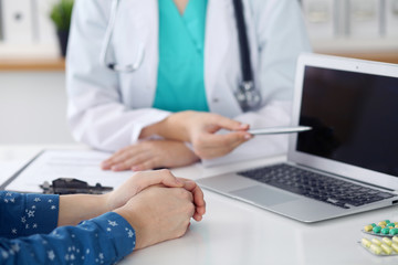  Close up of a doctor and  patient  sitting at the desk while physician pointing into laptop computer. Medicine and health care concept