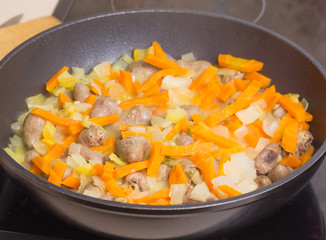 Fried chicken hearts with vegetables, carrots, onion, greens on a black frying pan, closed the glass cover. Background close-up. Prepare meals in the Kitchen.