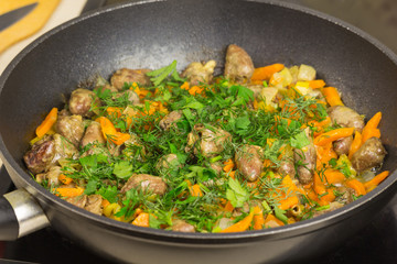 Fried chicken hearts with vegetables, carrots, onion, greens on a black frying pan, closed the glass cover. Background close-up. Prepare meals in the Kitchen.