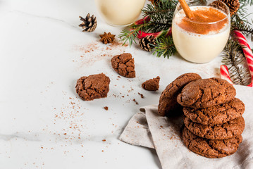Chocolate Crinkle cookies for Christmas, with eggnog cocktail, candy cane, Christmas tree and holiday decoration, on white marble table, copy space